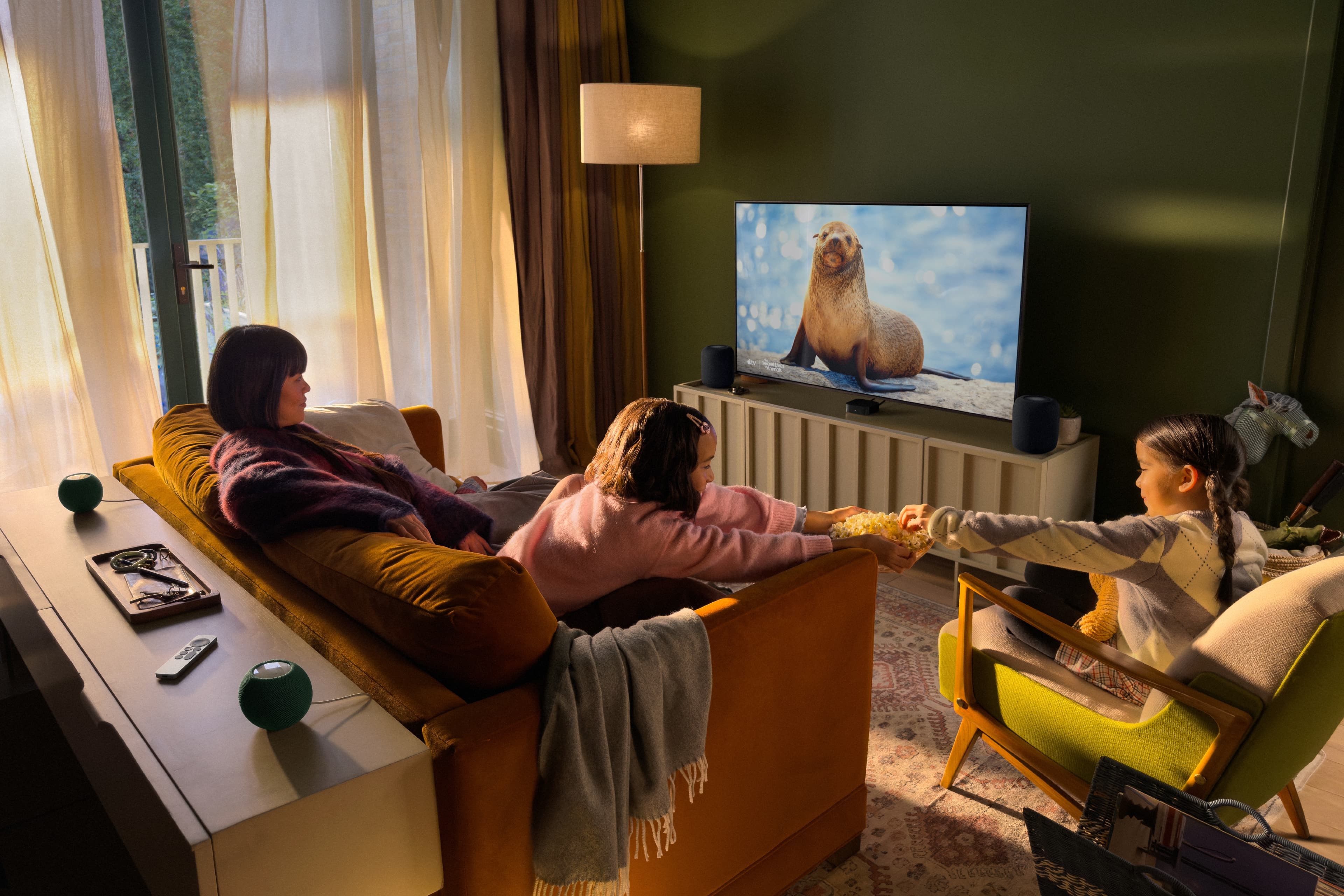 Apple's picture of the four-speaker setup: one pair of speakers either side of the TV and a pair of HomePod mini speakers behind the sofa. The front and rear pairs must each match. Image: Apple Newsroom.